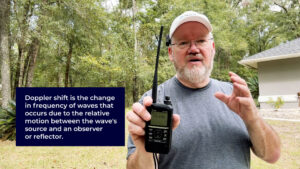 Ham radio operator holding a handheld transceiver while explaining Doppler shift for ISS passes; on-screen box defines Doppler shift and the radio is tuned near 145.800 MHz.