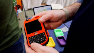 Orange LILYGO T-Deck Meshtastic device with touchscreen, physical keyboard, and LoRa antenna